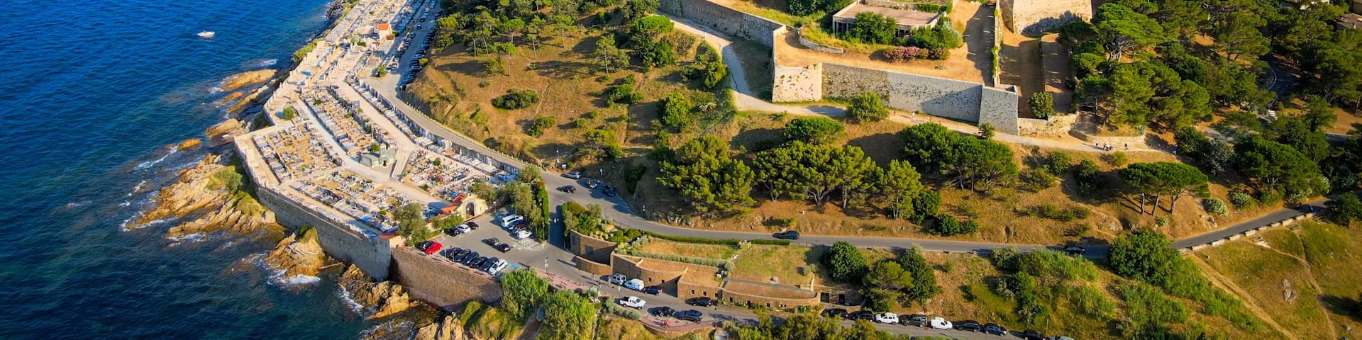 Un pueblo costero con una fortaleza histórica, un puerto deportivo con barcos y una zona residencial muy poblada.