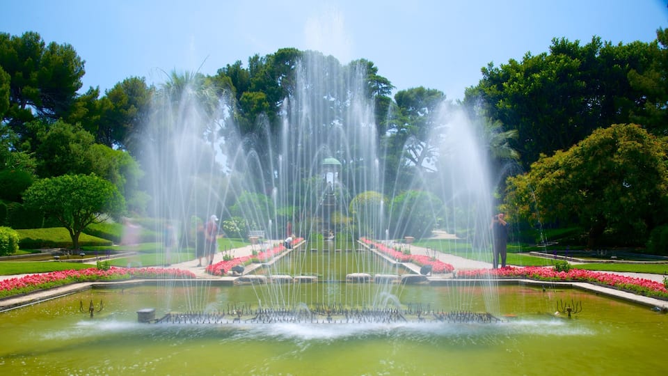 A large fountain with water jets in a park with trees and flower beds.
