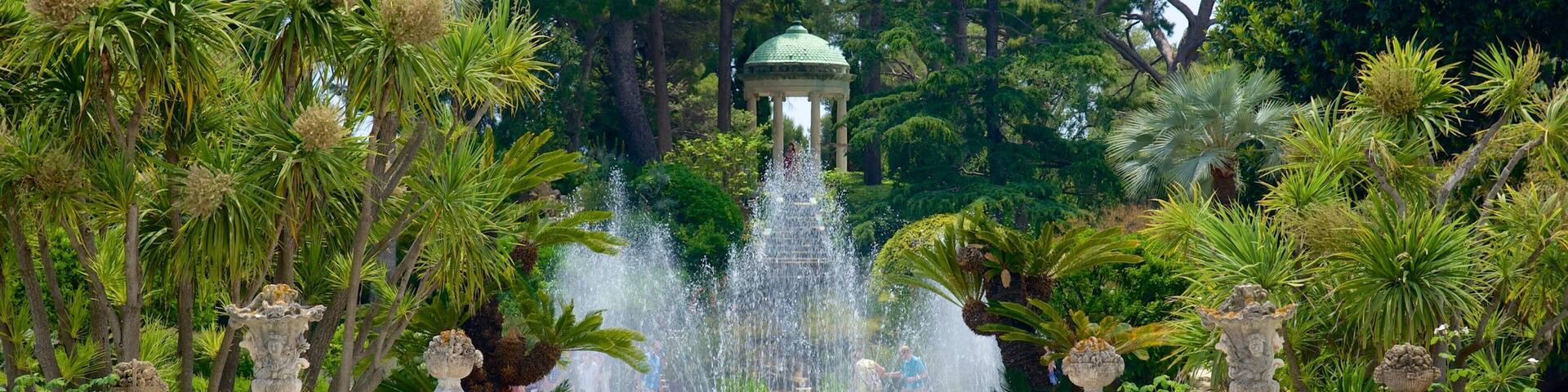 A fountain with water jets, surrounded by lush greenery and stone vases.