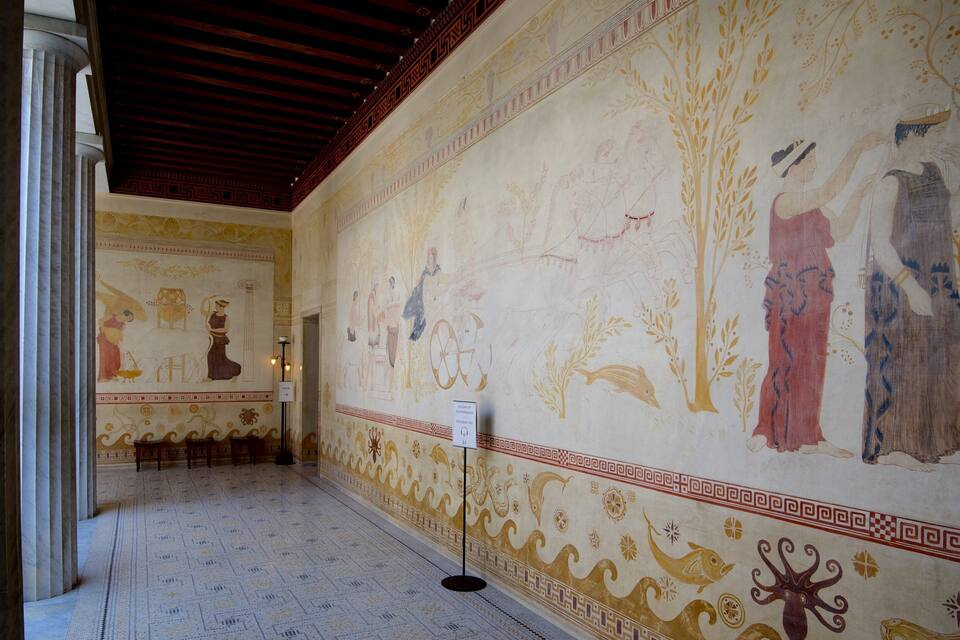 A corridor with ancient frescoes depicting mythological scenes and figures, marble columns, and a patterned floor.