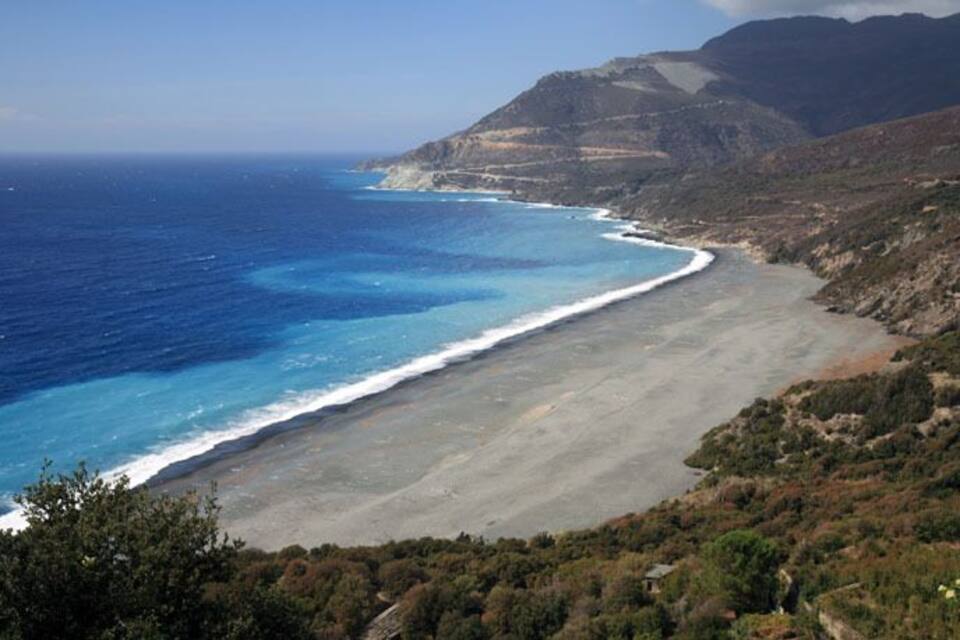 A coastal landscape with a beach, ocean, and mountainous terrain.