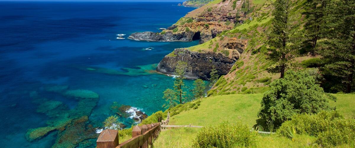 A coastal landscape with clear blue waters, rocky cliffs, and lush greenery.