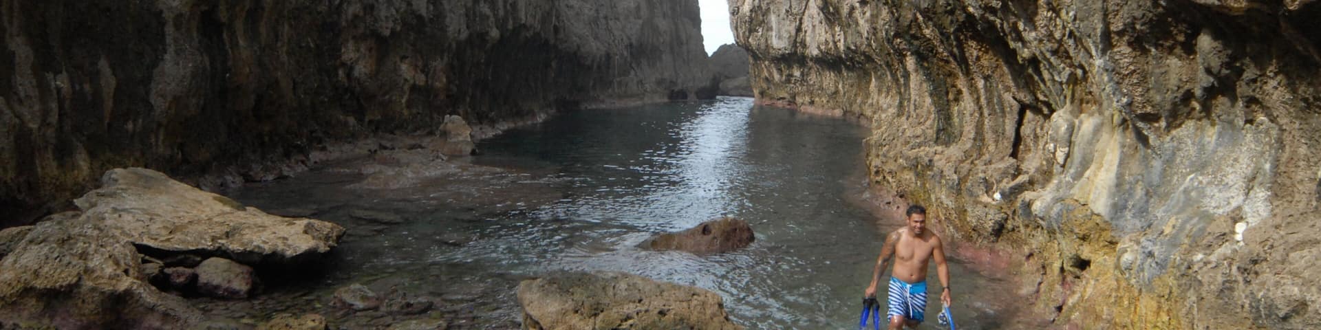 A man standing in a rocky riverbed surrounded by steep cliffs.