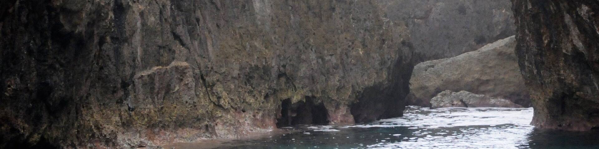 Un hombre salta desde un acantilado rocoso hacia una masa de agua rodeada de imponentes riscos.