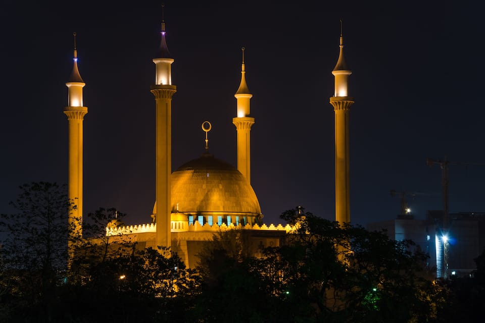 A mosque with four illuminated minarets and a large central dome at night.