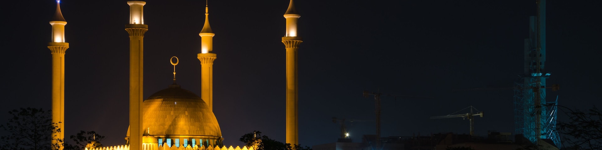 Uma mesquita com quatro minaretes e uma cúpula grande, rodeada por árvores e edifícios.