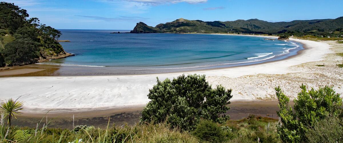 A coastal landscape with a sandy beach, clear blue waters, and green hills in the background.