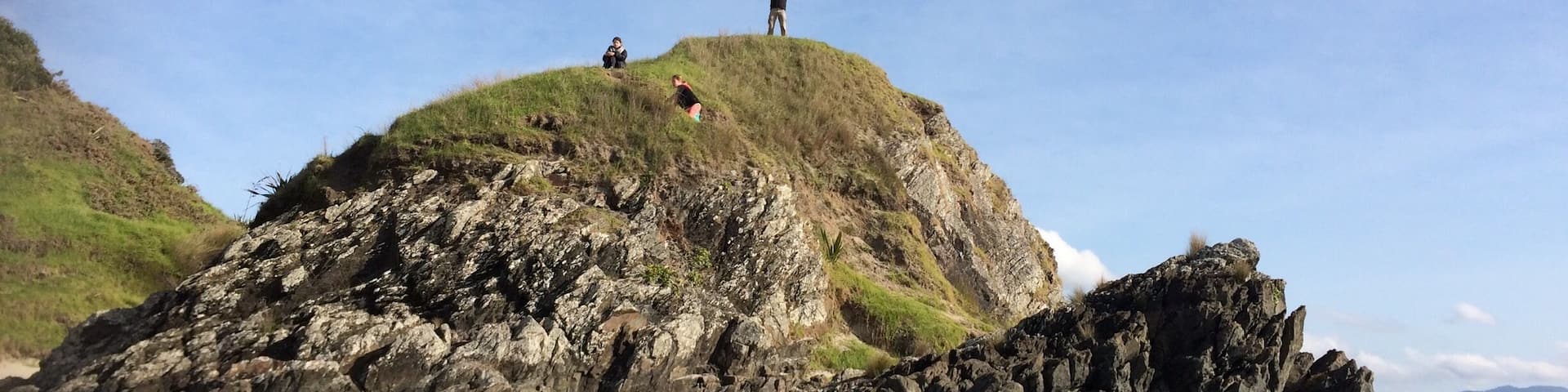 Une colline rocheuse avec des personnes au sommet, une plage au premier plan et un ciel bleu dégagé.