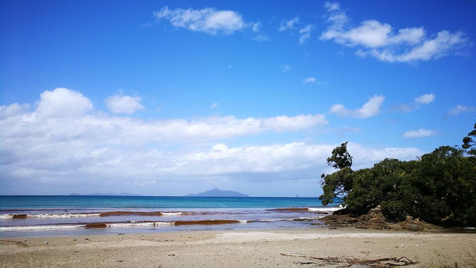 A beach with clear blue water, a sandy shore, and distant mountains.