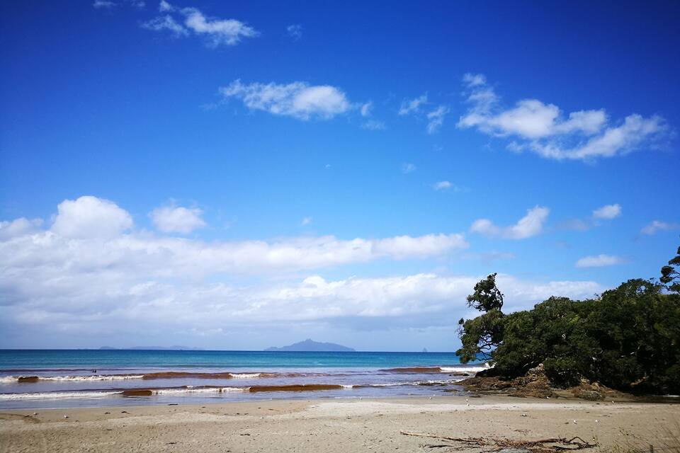 A beach with clear blue water, a sandy shore, and distant mountains.