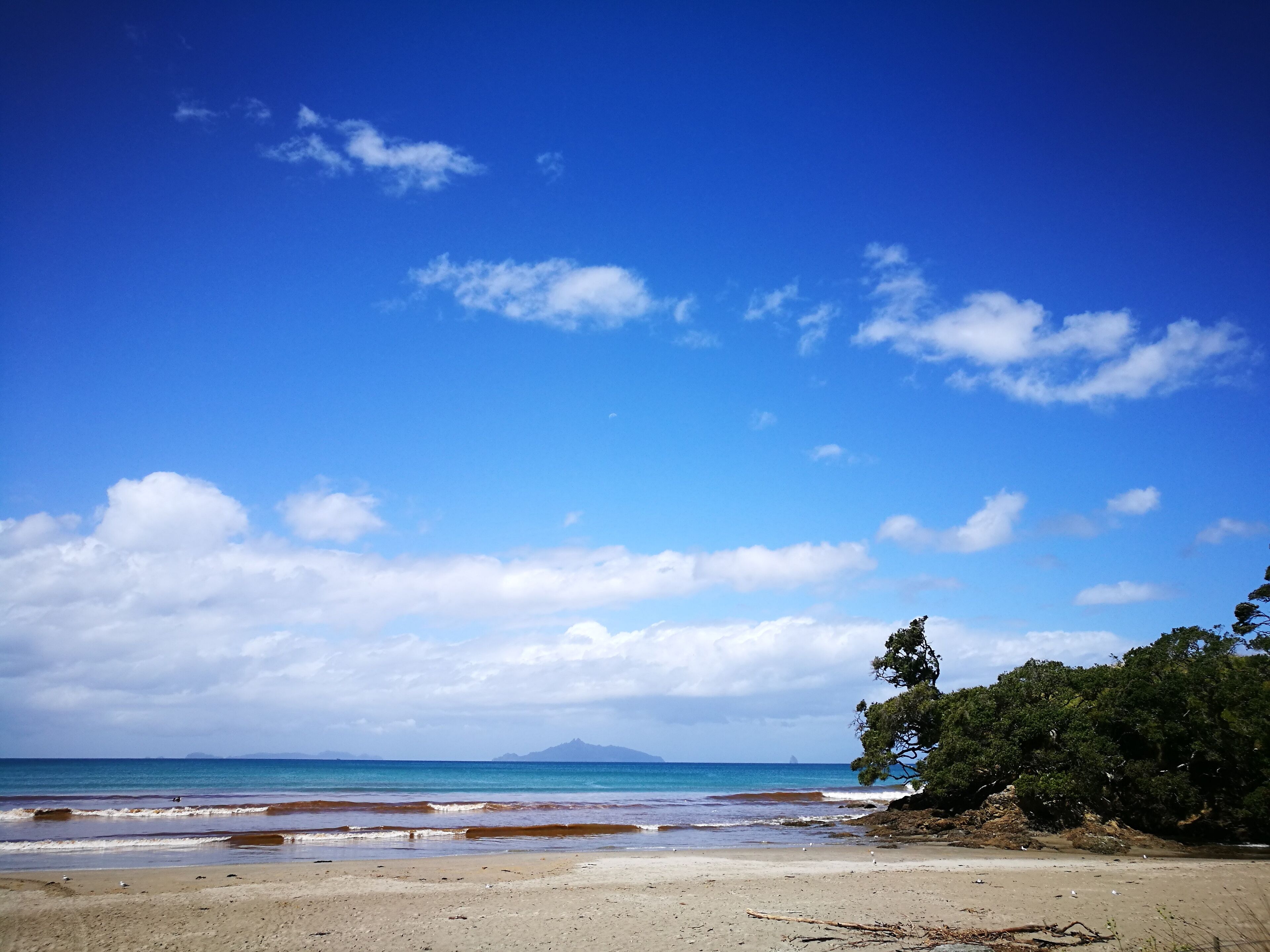 A beach with clear blue water, a sandy shore, and distant mountains.