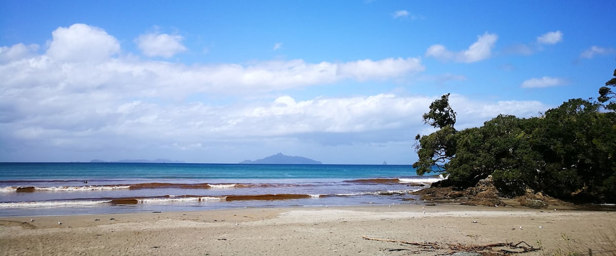 A beach with clear blue water, a sandy shore, and distant mountains.