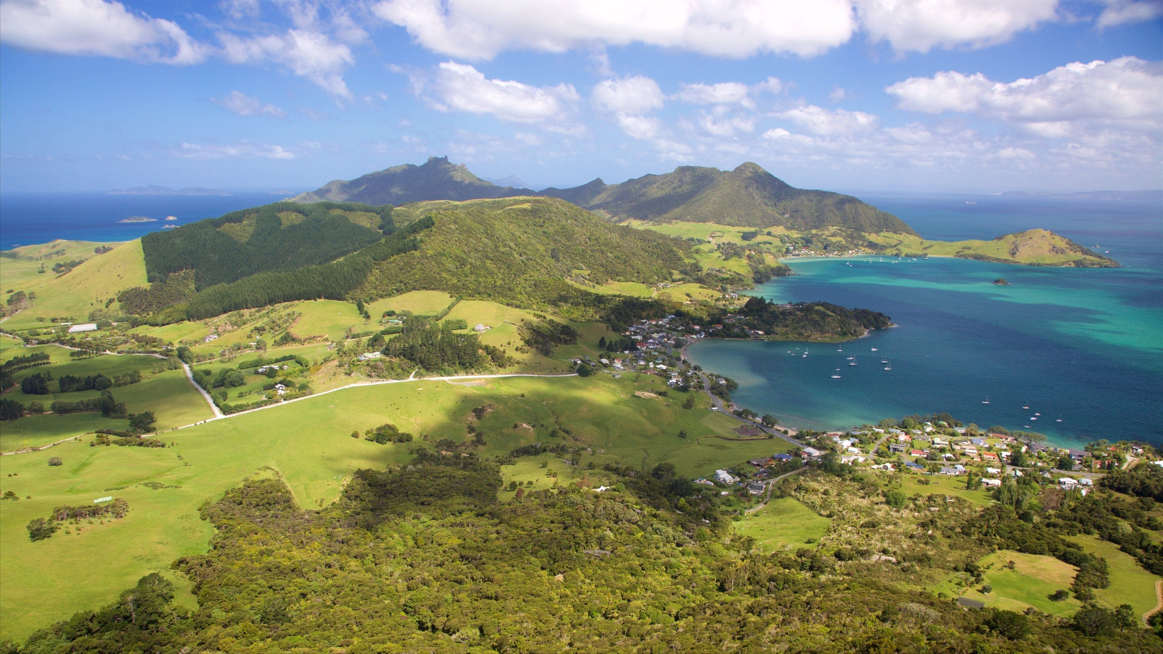Paisagem costeira com colinas verdes, uma pequena cidade e águas azul-claras com barcos.