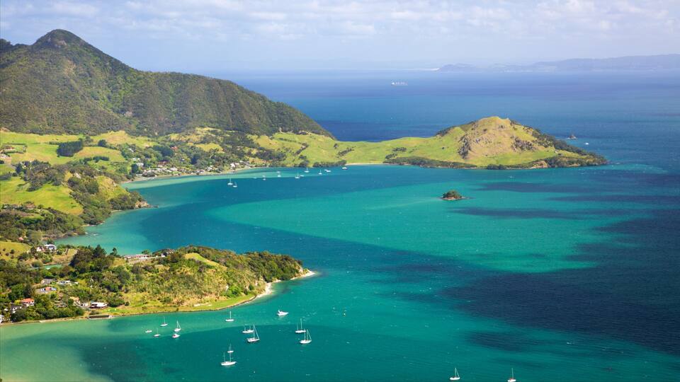 A coastal landscape with clear turquoise waters, a small island, and a mountainous backdrop.