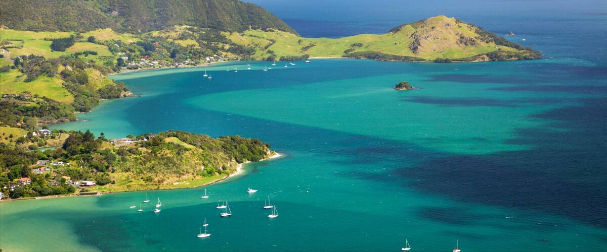 A coastal landscape with clear turquoise waters, a small island, and a mountainous backdrop.