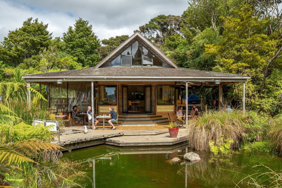 A wooden building with a glass front, surrounded by lush greenery and a pond.