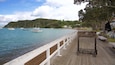 Un muelle de madera con un letrero que dice "Kororareka" que da vista a un puerto tranquilo con varios barcos.