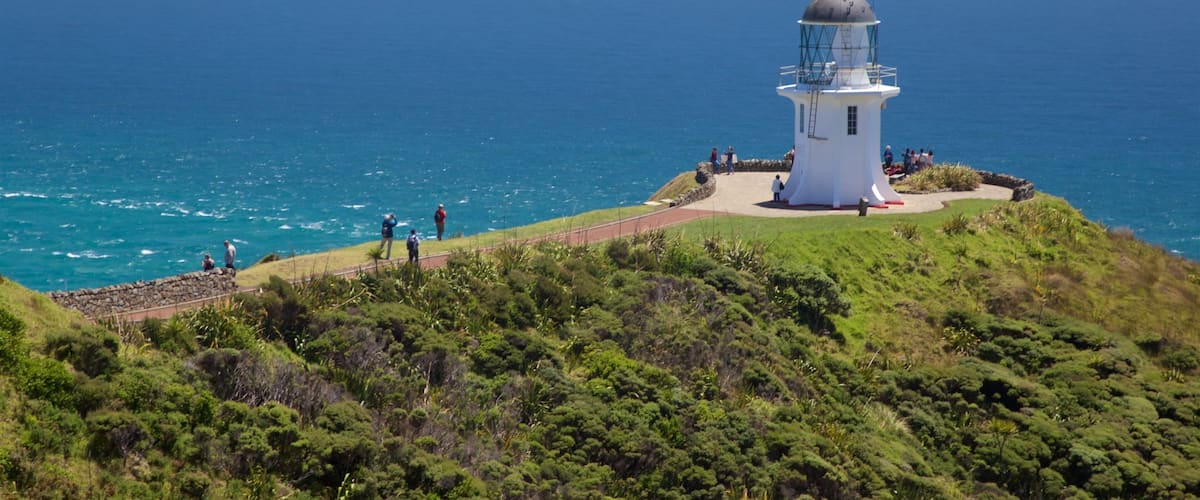 A lighthouse on a grassy hill overlooking the ocean.