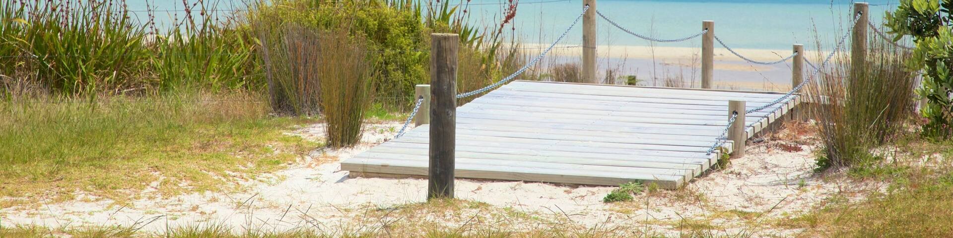 A beach with a wooden boardwalk leading to a lifeguard tower.