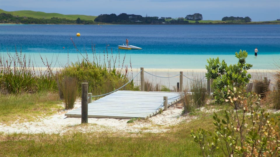 A beach with a wooden boardwalk leading to the water, a lifeguard tower, and a clear blue ocean.