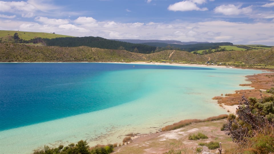 A coastal landscape with clear turquoise waters, sandy beaches, and rolling hills covered in greenery.