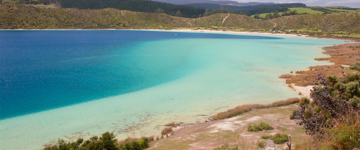 A coastal landscape with clear turquoise waters, sandy beaches, and rolling hills covered in greenery.