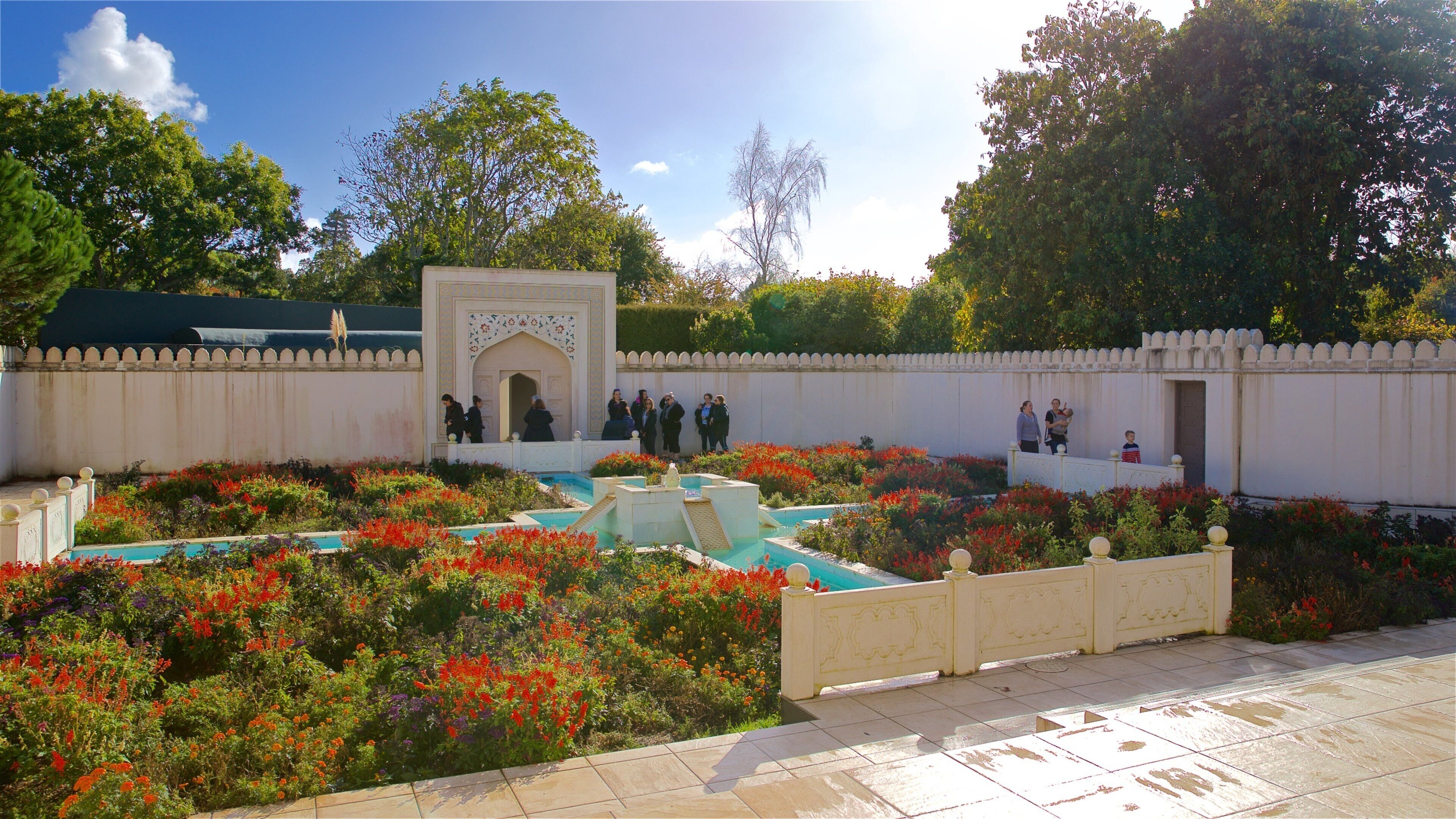 Un jardín con una fuente, un muro blanco y un grupo de personas.