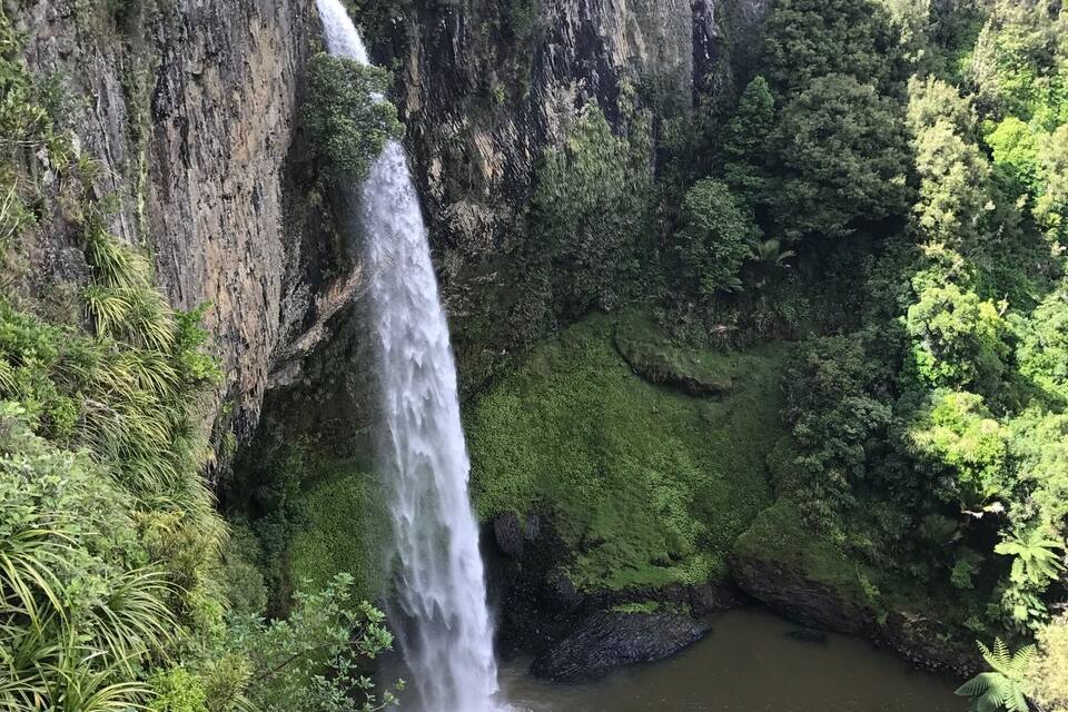 Uma cascata despencando de um penhasco, cercada por vegetação exuberante.