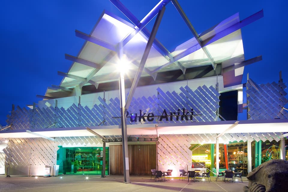 Um edifício moderno com fachada geométrica única e o nome "Puke Ariki" em destaque.