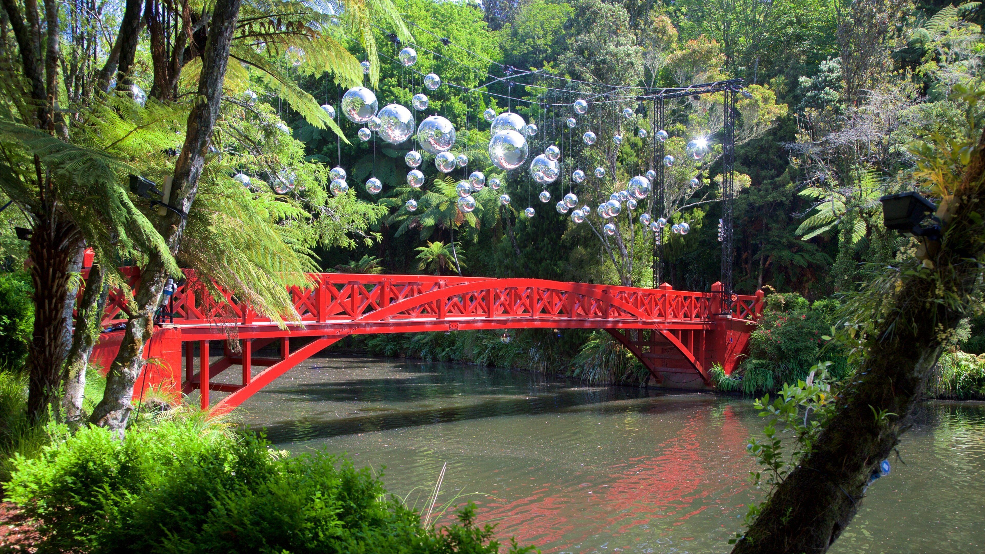 Un pont rouge enjambant une rivière, avec des sphères réfléchissantes suspendues au-dessus.
