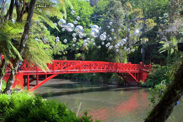 A red bridge over a river with reflective spheres hanging above.