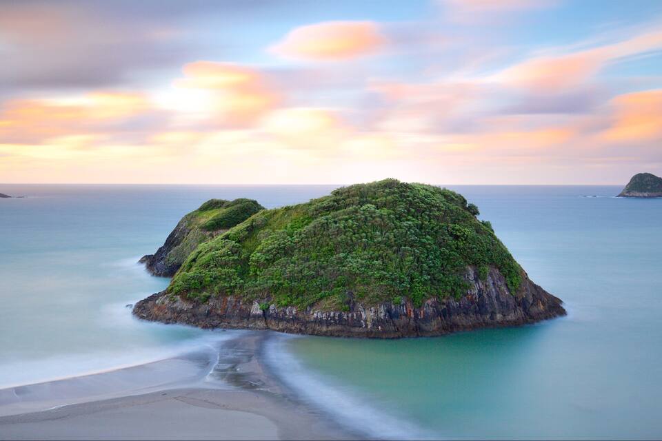 A coastal landscape with two prominent green islands surrounded by calm sea and a beach.