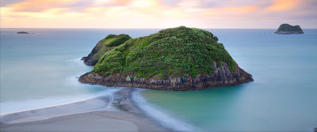 A coastal landscape with two prominent green islands surrounded by calm sea and a beach.