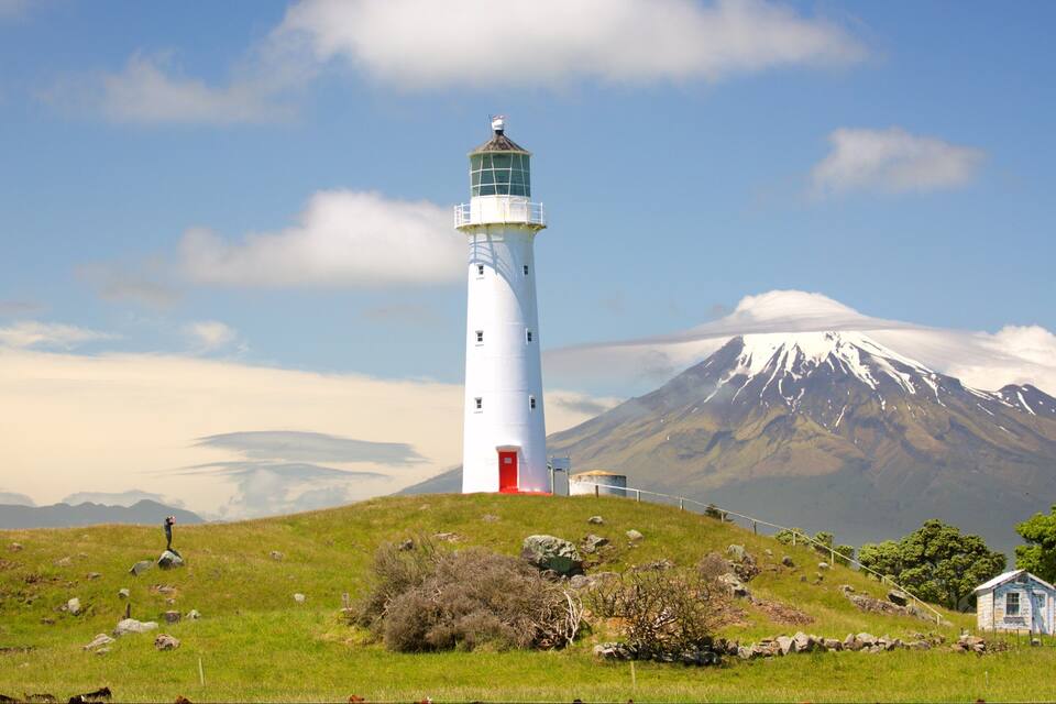 A lighthouse on a grassy hill with a snow-capped mountain in the background.