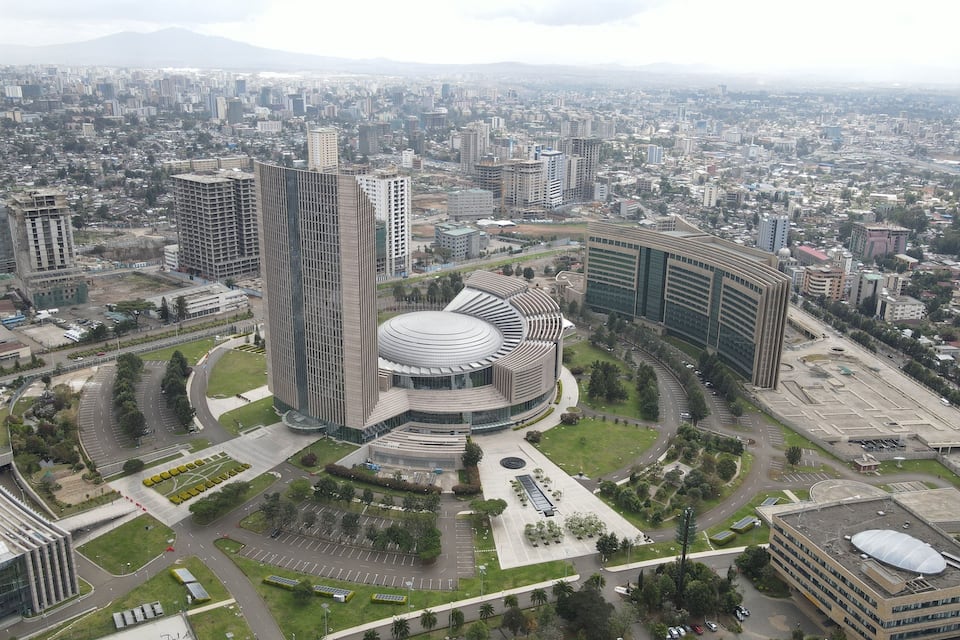 Un paisaje urbano con un edificio circular destacado, rodeado de modernos rascacielos, carreteras y zonas verdes.