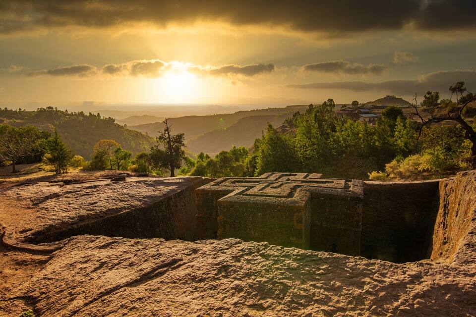 Una estructura de piedra con tallas, rodeada por un paisaje montañoso y un atardecer.