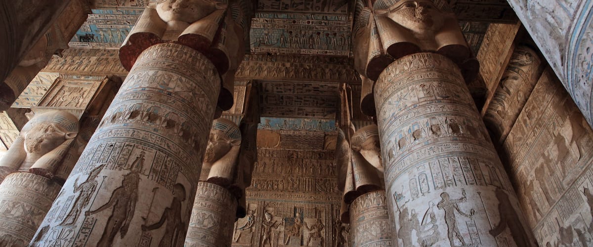 Ancient Egyptian columns with hieroglyphs and a ceiling with detailed artwork.