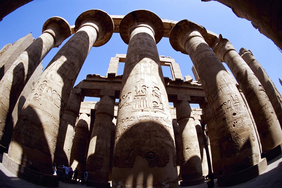 Columnas egipcias antiguas con jeroglíficos, parte de una estructura de templo más grande.