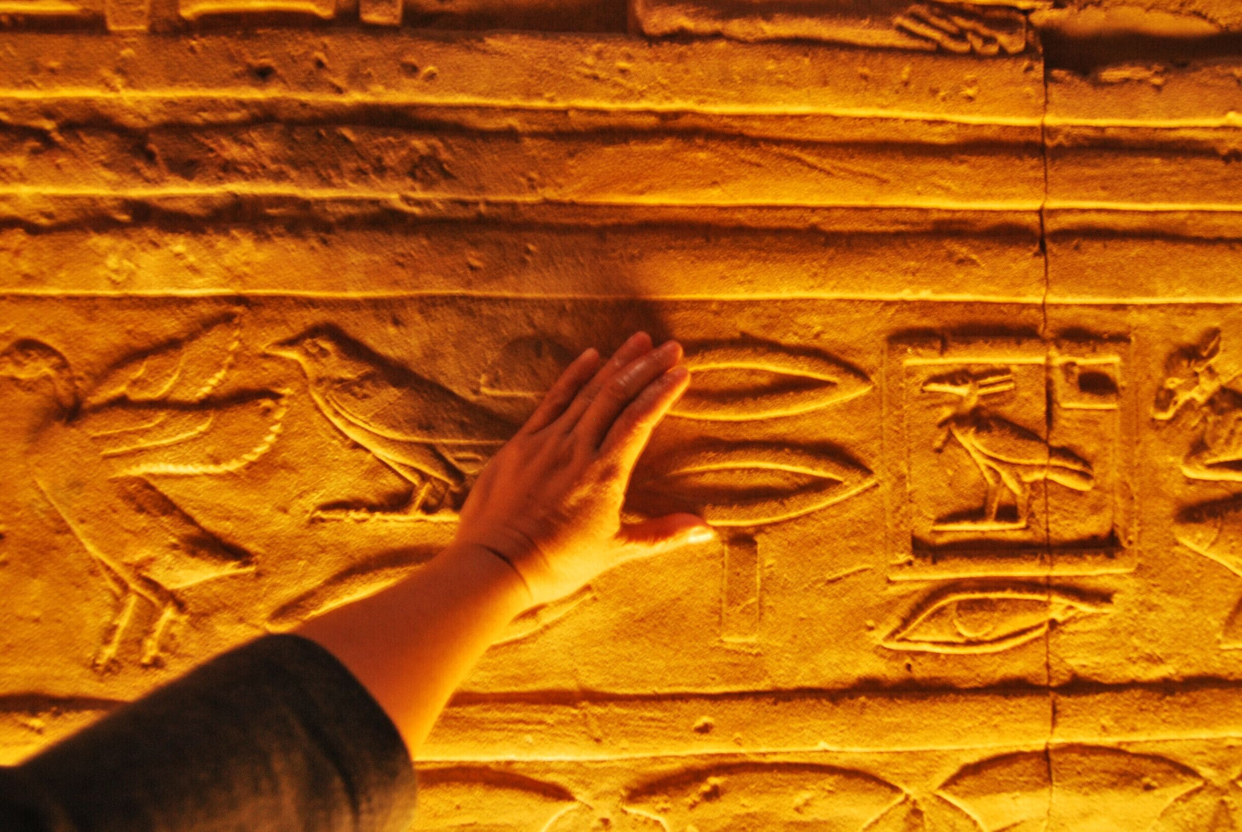 A hand touching ancient carvings on a wall.