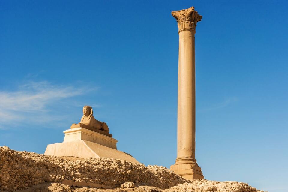 A large column and a statue in a desert landscape.