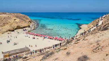 Una playa costera con aguas turquesas cristalinas, una orilla arenosa y acantilados rocosos.