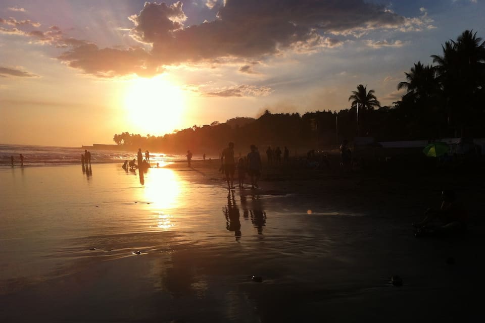 Una playa al atardecer con gente caminando y jugando en el agua.
