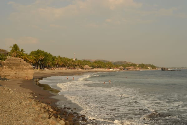 A beach with palm trees, a rocky shoreline, and a calm sea.