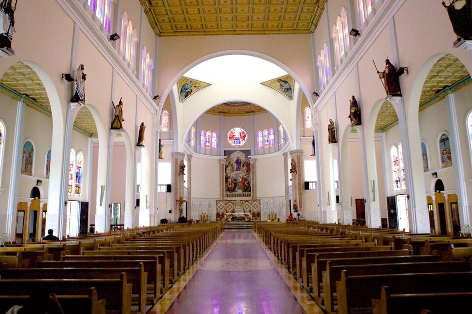 An interior of a church with rows of wooden pews, stained glass windows, and religious statues.