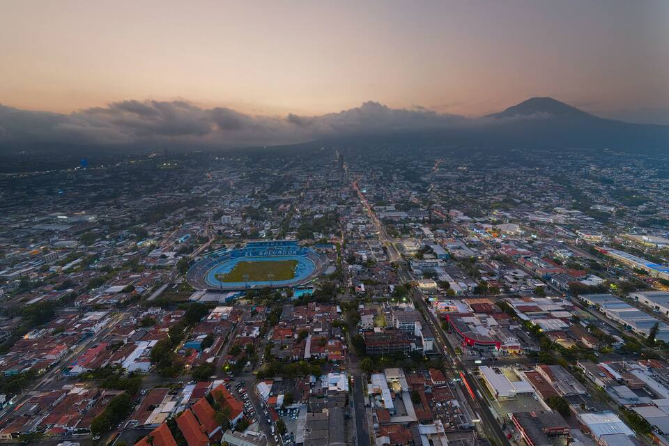 An aerial view of a city with a stadium named 'El Salvador' and a mountain in the background.