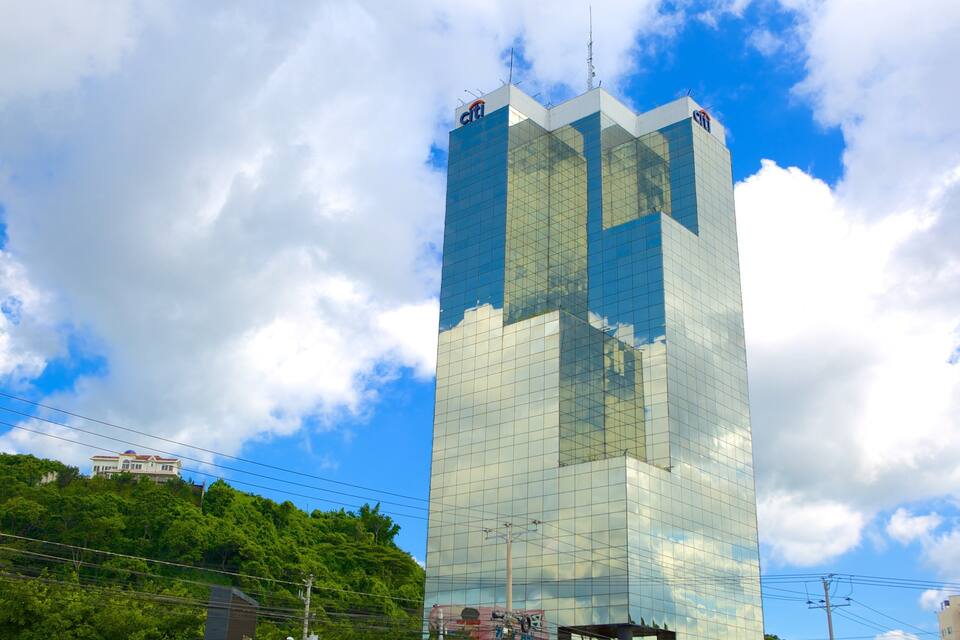 A tall glass building with the Citi logo, surrounded by lush greenery and a partly cloudy sky.