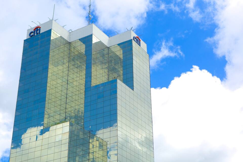 A tall glass building with the Citi logo, reflecting clouds and sky.