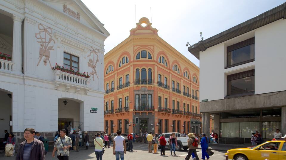 Eine belebte Stadtstraße mit historischen Gebäuden, darunter ein Gebäude in Rosa und Weiß mit Balkonen und ein weißes Gebäude mit einer verzierten Fassade.