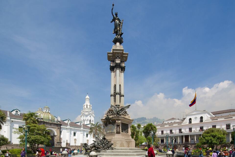 A monument with a statue, surrounded by buildings and palm trees.