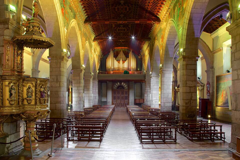 An ornate church interior with rows of pews, a large organ, and intricate ceiling artwork.